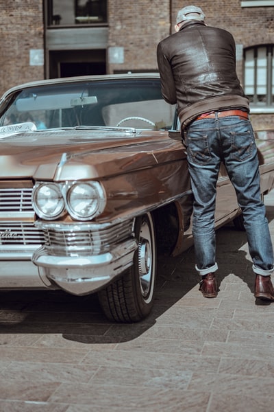 一个穿着蓝色牛仔裤的男人站在棕色汽车旁边